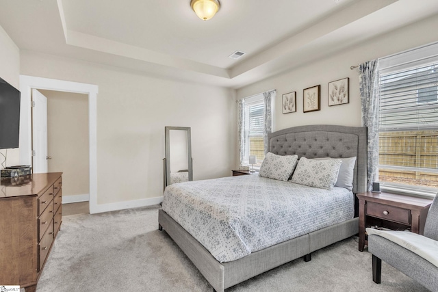 bedroom featuring light carpet, baseboards, visible vents, and a tray ceiling