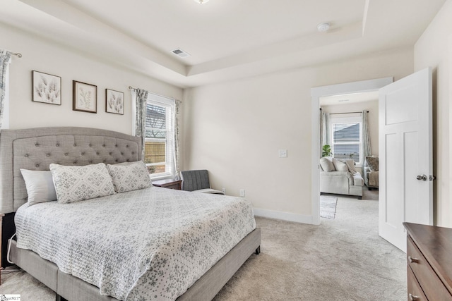 bedroom featuring light carpet, a tray ceiling, visible vents, and baseboards