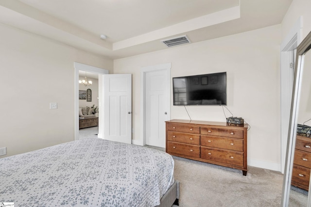 bedroom with an inviting chandelier, visible vents, a tray ceiling, and light colored carpet