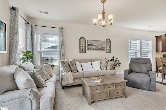 living area featuring a healthy amount of sunlight, light carpet, visible vents, and a notable chandelier