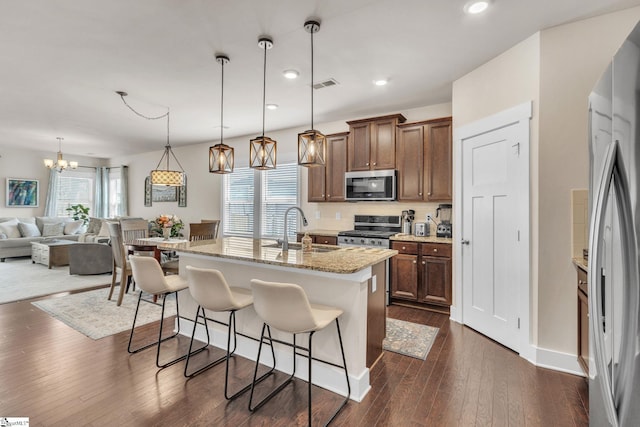 kitchen featuring visible vents, appliances with stainless steel finishes, a kitchen breakfast bar, dark wood-type flooring, and a sink