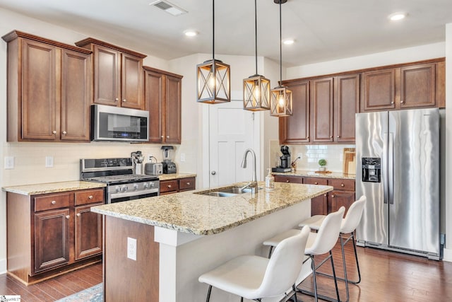 kitchen featuring a sink, visible vents, appliances with stainless steel finishes, dark wood-style floors, and a center island with sink