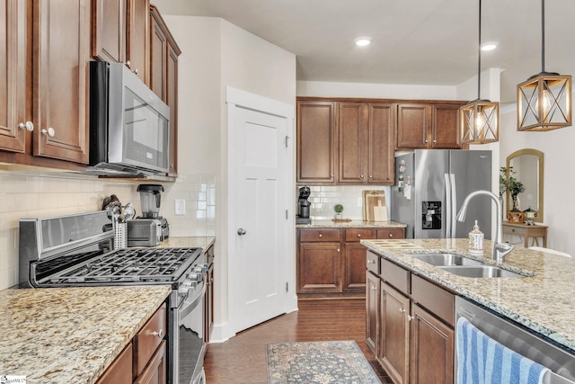 kitchen featuring light stone counters, brown cabinets, stainless steel appliances, hanging light fixtures, and a sink