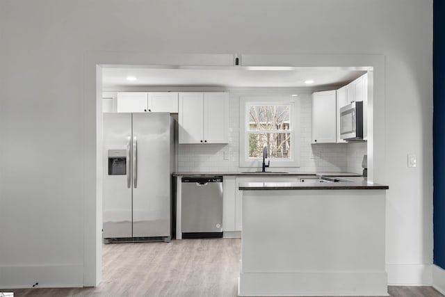 kitchen with appliances with stainless steel finishes, backsplash, a sink, and light wood-style floors