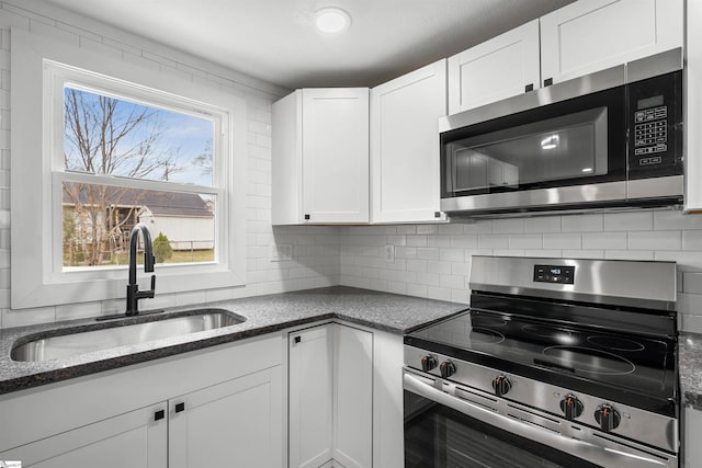 kitchen with stainless steel appliances, a sink, white cabinetry, decorative backsplash, and dark stone counters