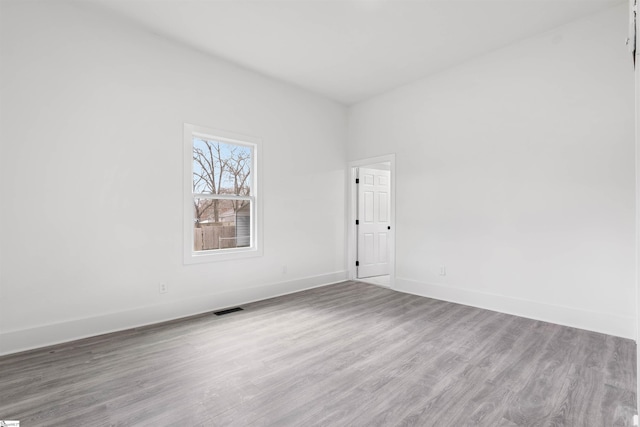 spare room featuring wood finished floors, visible vents, and baseboards