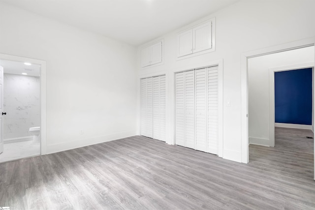 unfurnished bedroom with ensuite bathroom, baseboards, and wood finished floors