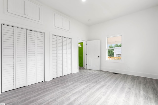 unfurnished bedroom with light wood-type flooring, visible vents, baseboards, and two closets