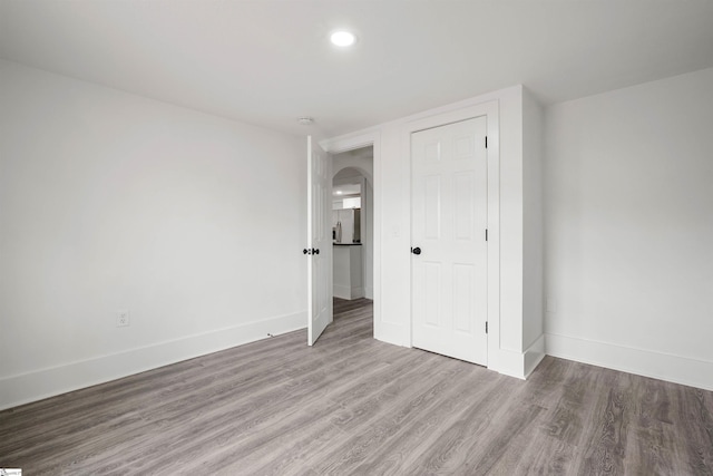 unfurnished bedroom with arched walkways, a closet, wood finished floors, and baseboards