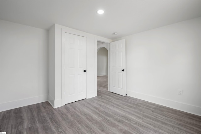 unfurnished bedroom featuring arched walkways, recessed lighting, wood finished floors, baseboards, and a closet