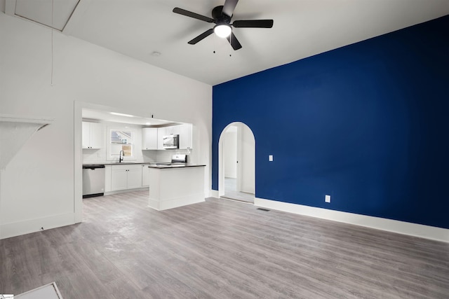 unfurnished living room featuring arched walkways, ceiling fan, a sink, light wood-style floors, and attic access