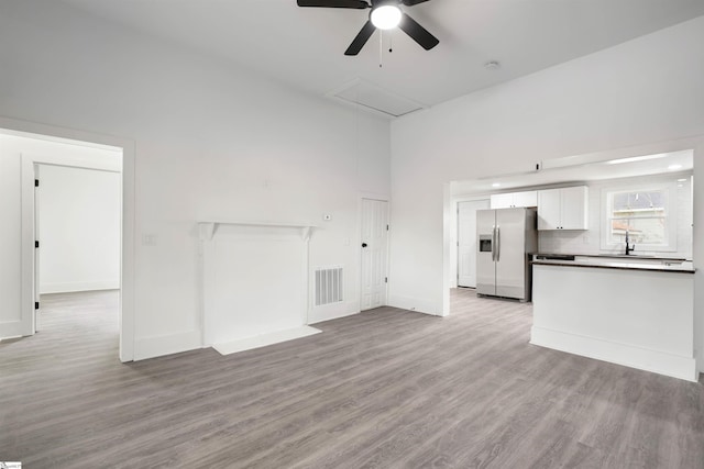 unfurnished living room with light wood finished floors, attic access, visible vents, a towering ceiling, and a sink