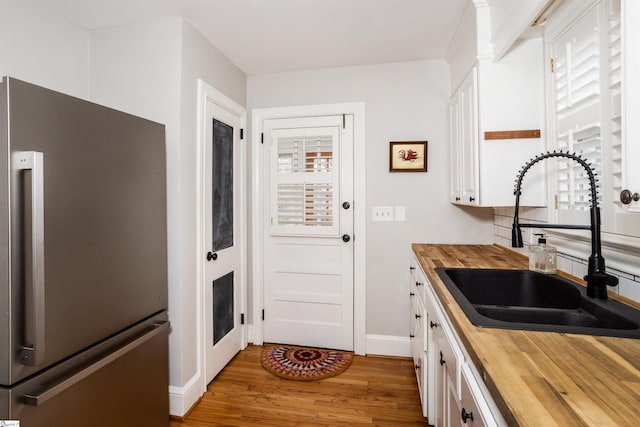 kitchen featuring freestanding refrigerator, white cabinets, a sink, wood counters, and wood finished floors