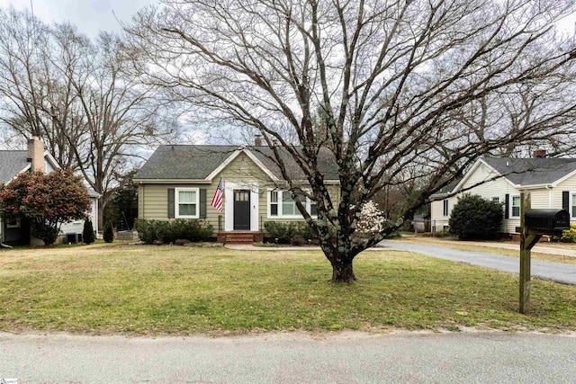 bungalow with roof with shingles, a chimney, and a front lawn