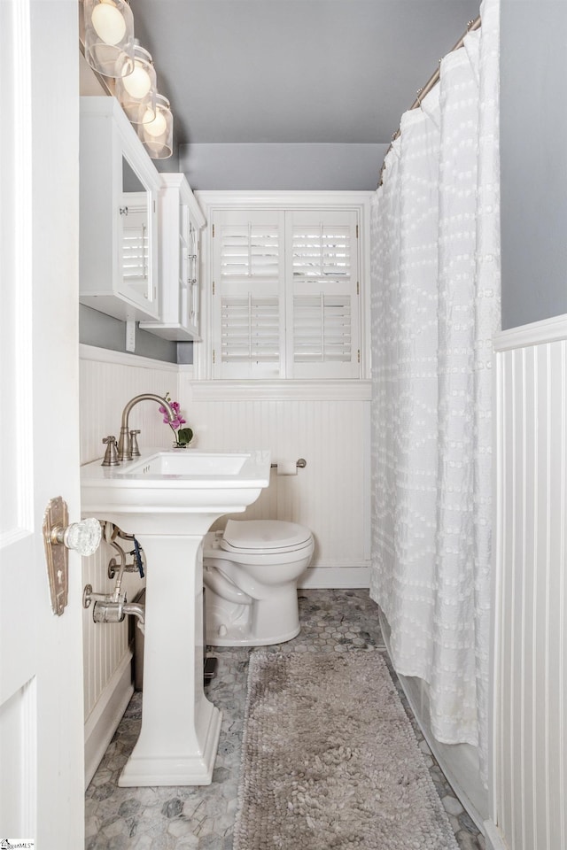 bathroom with toilet, wainscoting, and a shower with shower curtain