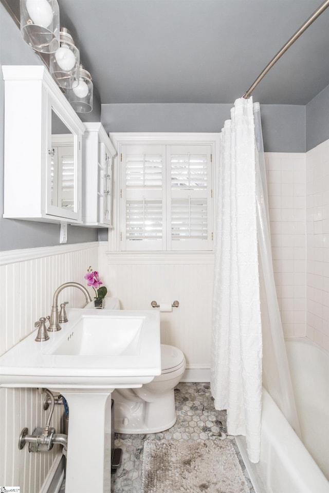 full bath with a wainscoted wall, shower / bath combination with curtain, and toilet