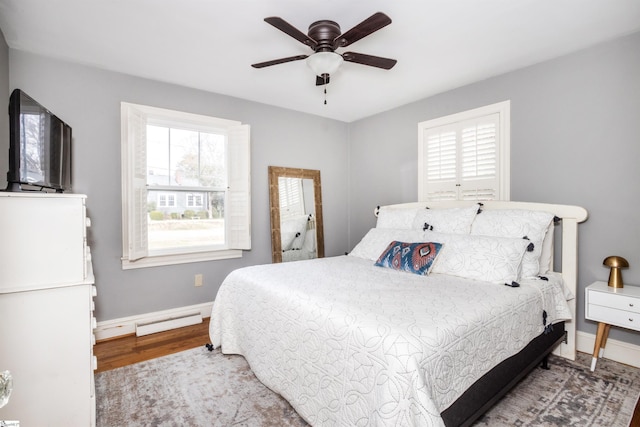 bedroom with a baseboard heating unit, multiple windows, wood finished floors, and baseboards