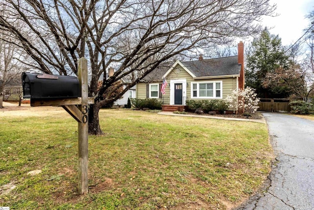 view of front of home with aphalt driveway, a chimney, a front yard, and fence