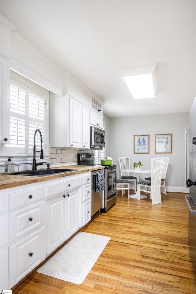 kitchen with a skylight, light wood finished floors, appliances with stainless steel finishes, white cabinets, and a sink