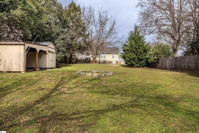 view of yard with a fire pit, a storage shed, fence, and an outbuilding