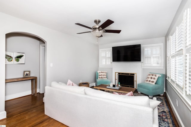 living area featuring arched walkways, a fireplace, wood finished floors, and baseboards