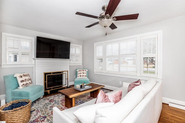 living room with a baseboard heating unit, a brick fireplace, wood finished floors, and baseboards