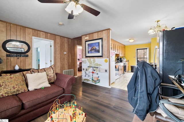 living room featuring visible vents, wood walls, light wood-style flooring, and ceiling fan with notable chandelier