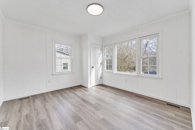 empty room with baseboards, visible vents, wood finished floors, and ornamental molding