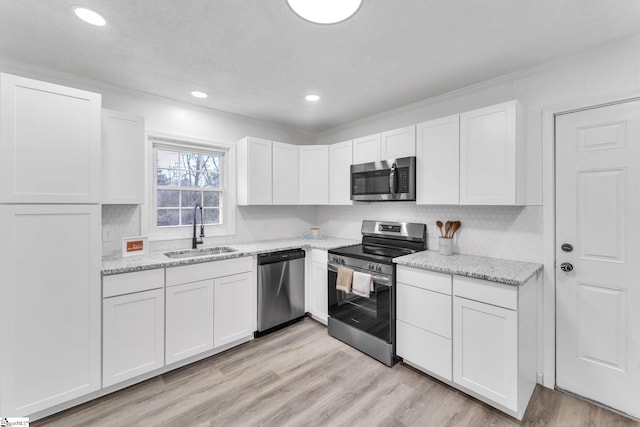 kitchen featuring stainless steel appliances, white cabinetry, a sink, and light wood finished floors