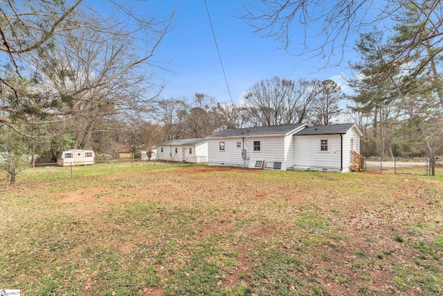 rear view of house featuring a yard, crawl space, an outdoor structure, and fence