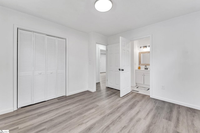 unfurnished bedroom featuring ornamental molding, a closet, a sink, and light wood-style flooring