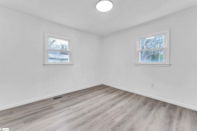 empty room with plenty of natural light, wood finished floors, and visible vents