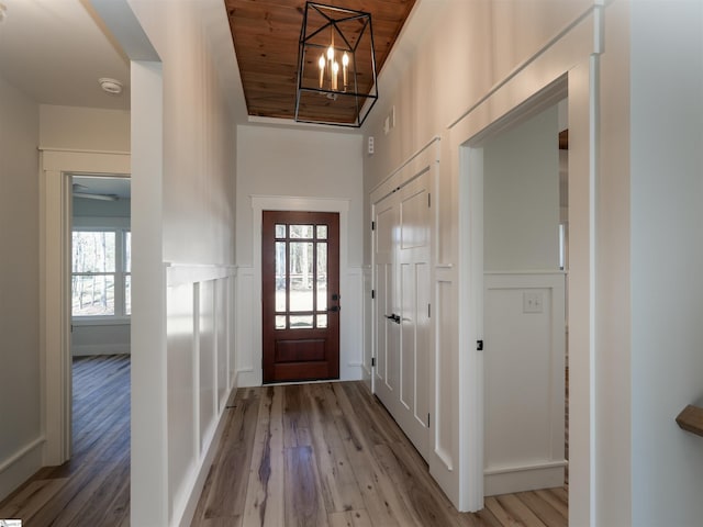 foyer entrance with wooden ceiling, a wainscoted wall, a decorative wall, and wood finished floors