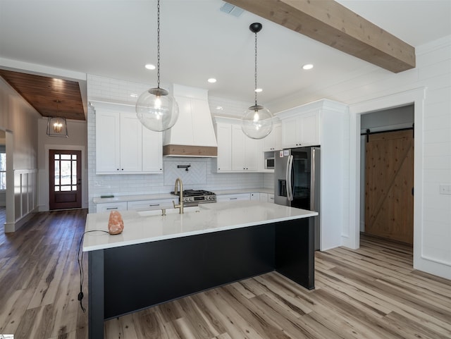 kitchen with a barn door, tasteful backsplash, visible vents, custom range hood, and light wood-type flooring