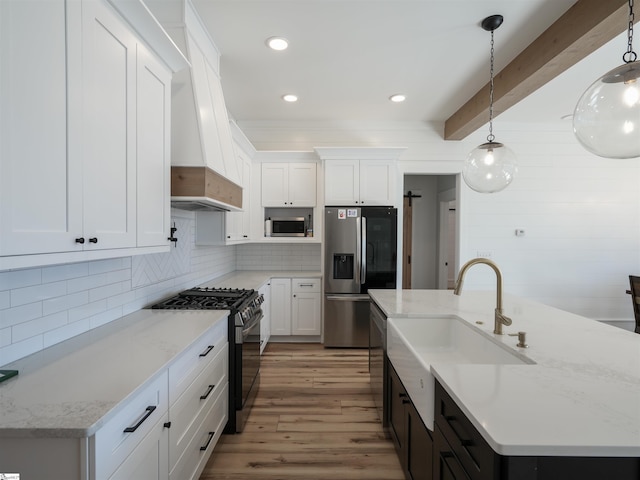 kitchen featuring stainless steel appliances, custom range hood, white cabinetry, a sink, and wood finished floors