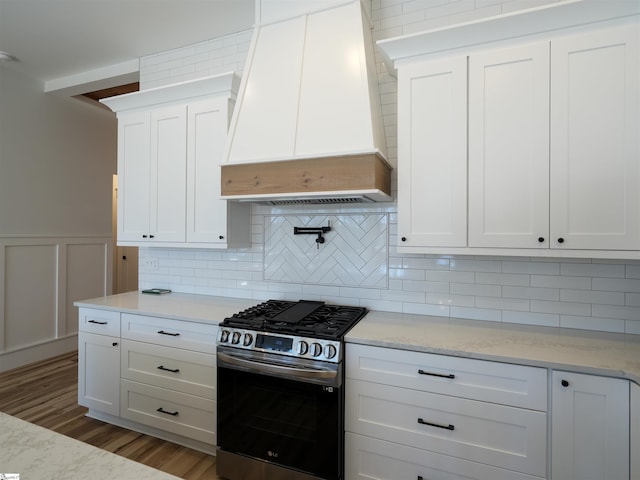 kitchen featuring light wood-style flooring, premium range hood, white cabinetry, decorative backsplash, and gas range