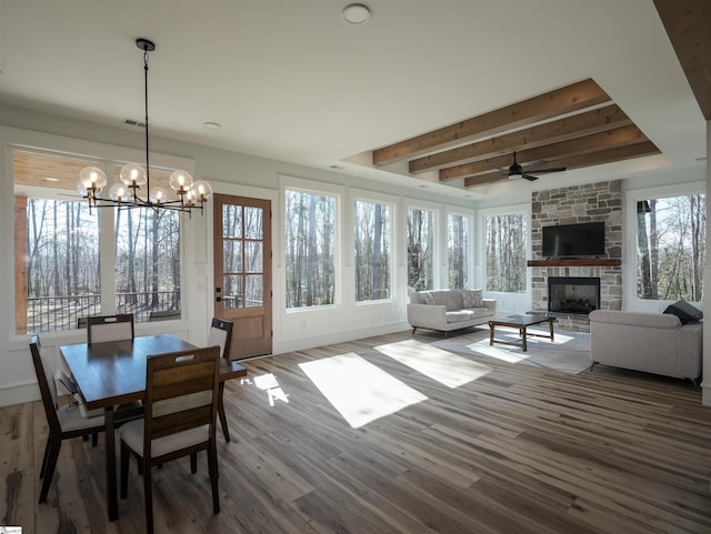 dining space with beam ceiling, visible vents, a stone fireplace, wood finished floors, and ceiling fan with notable chandelier