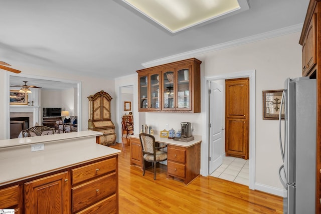 kitchen featuring glass insert cabinets, freestanding refrigerator, light countertops, light wood-type flooring, and a fireplace