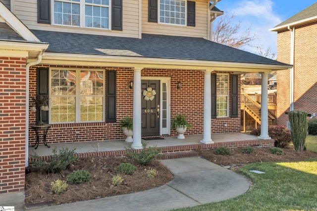 view of exterior entry with a shingled roof, a porch, and brick siding