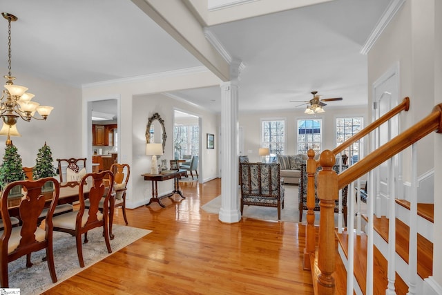 entrance foyer with decorative columns, stairway, ornamental molding, light wood-type flooring, and ceiling fan with notable chandelier