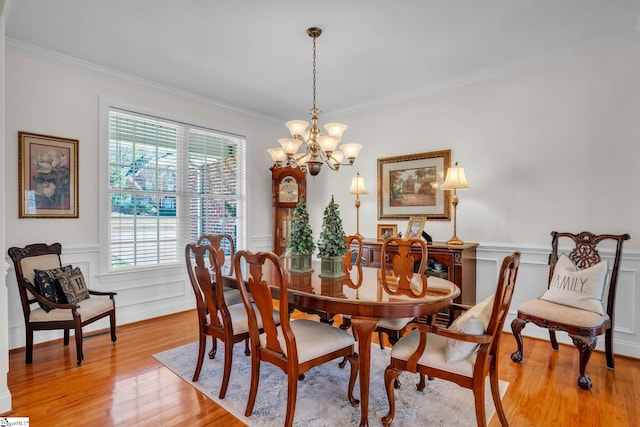 dining space with light wood-type flooring, wainscoting, a notable chandelier, and crown molding