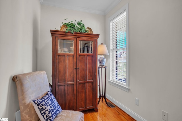 living area featuring baseboards, light wood-type flooring, visible vents, and crown molding