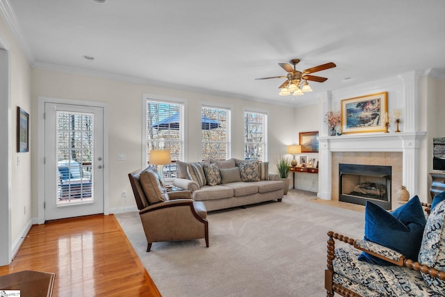 living area featuring a fireplace, crown molding, light wood-style flooring, ceiling fan, and baseboards