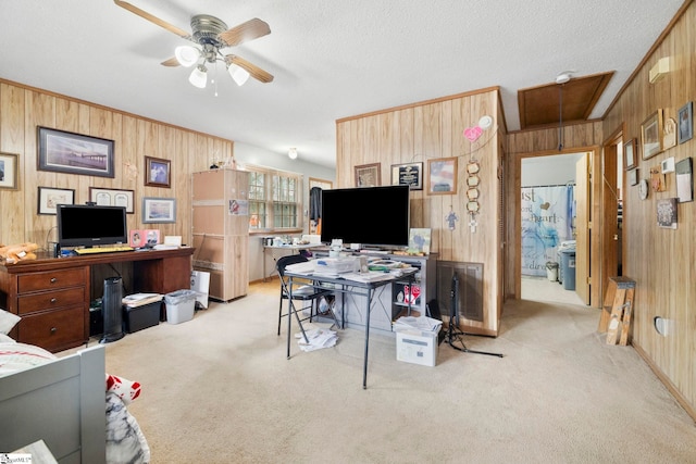 carpeted office space featuring wood walls, attic access, a textured ceiling, and a ceiling fan