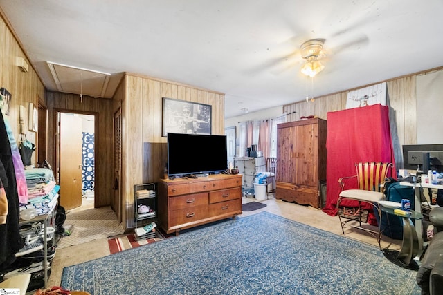 living area with attic access, wooden walls, and ceiling fan