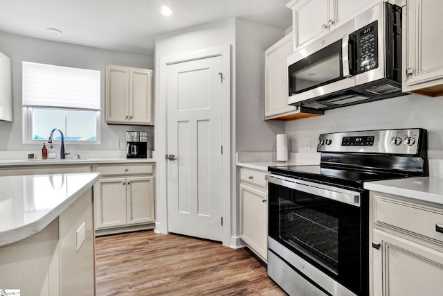 kitchen featuring a sink, white cabinets, light wood-style floors, light countertops, and appliances with stainless steel finishes