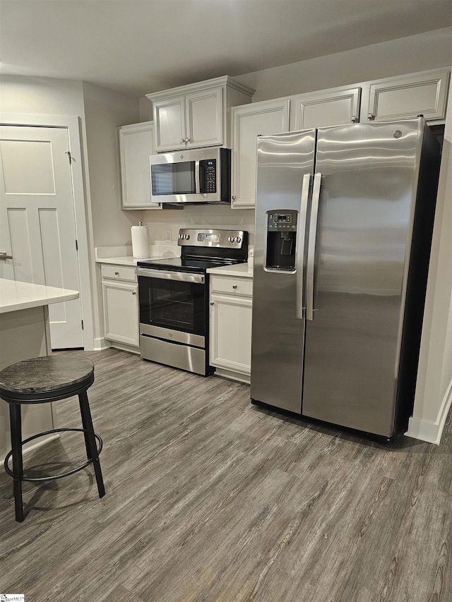 kitchen with light countertops, appliances with stainless steel finishes, wood finished floors, and white cabinetry