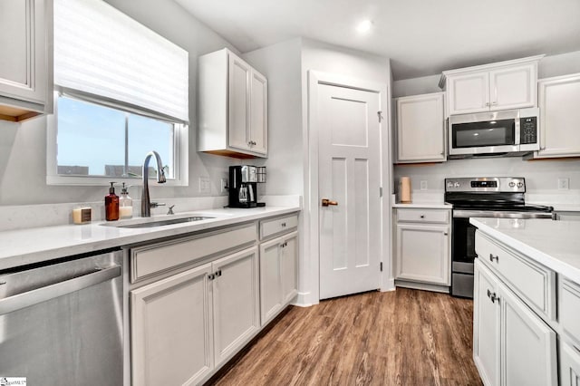 kitchen featuring stainless steel appliances, light countertops, light wood-style flooring, white cabinetry, and a sink