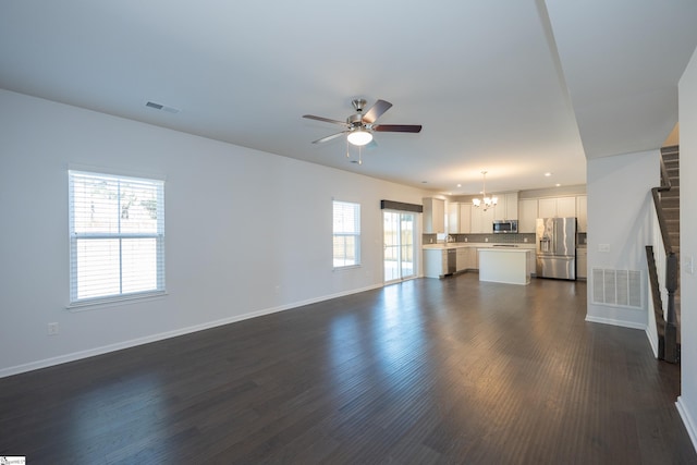 unfurnished living room featuring ceiling fan with notable chandelier, dark wood-type flooring, visible vents, and baseboards