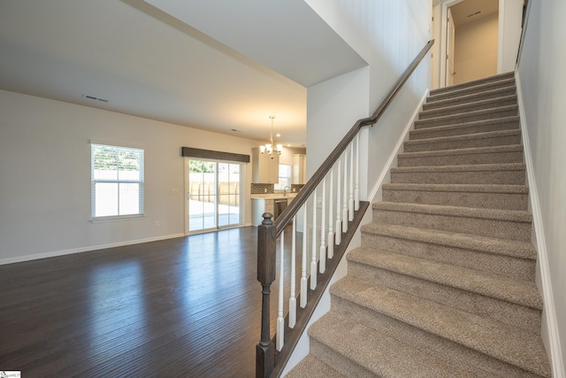 stairs featuring an inviting chandelier, baseboards, visible vents, and wood finished floors